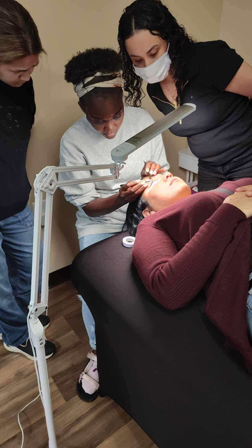 Students learning application techniques from the digital lash manual at Vela Lash Bar training session