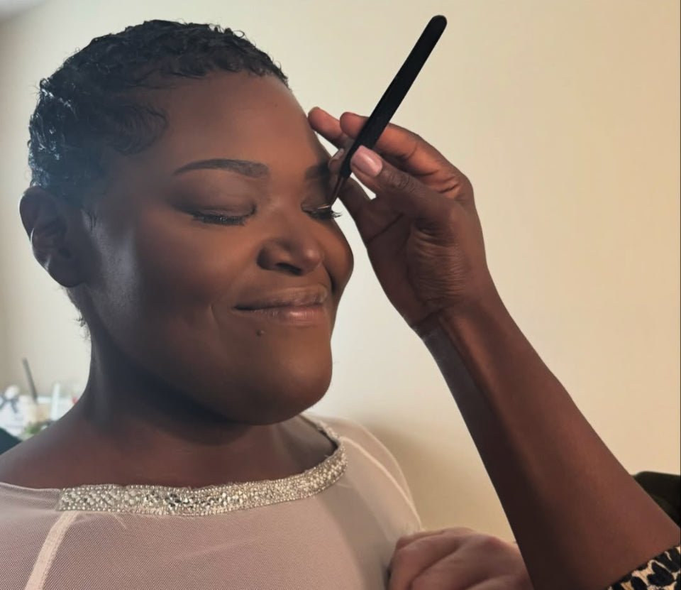 Applying eyeshadow with a brush on a smiling woman for wedding makeup services by Vela Lash Bar